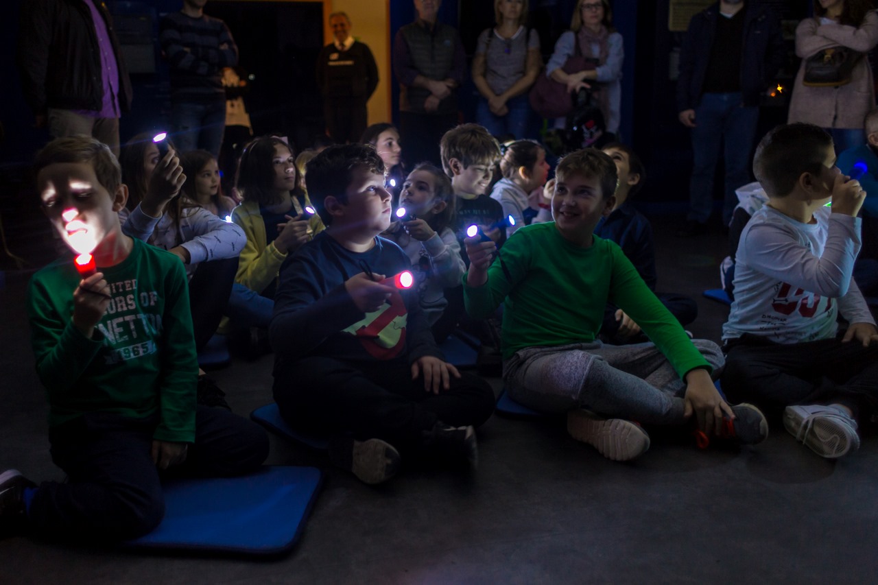 Museum in the dark - Παιδιά κάθονται στο πάτωμα και κρατούν φακούς